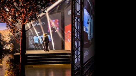 VISUELL Szenografie: BEST CARS 2023, in einer neuen Dimension mit sieben Leinwänden für ein 360° Gefühl VISUELL Szenografie: BEST CARS 2023: Eine große Bühne, auf der zwei Männer stehen umgeben von Pflanzen