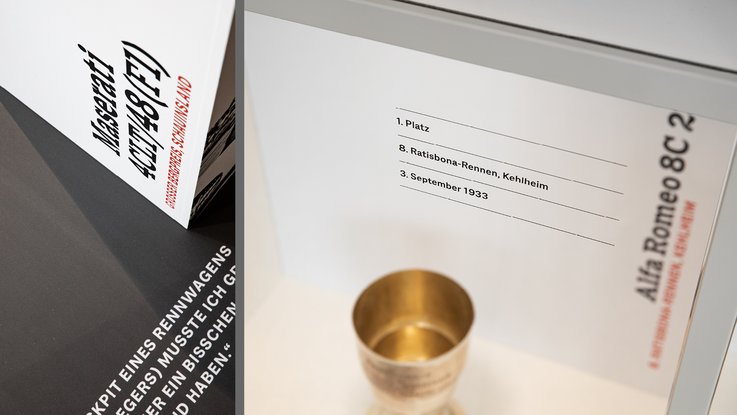 VISUELL Szenografie: Jubiläumsausstellung: Vom Rennfahrer zum Verleger, 75 Jahre Verlagsgeschichte VISUELL Szenografie: Ausstellungsrundgang: Detailansicht Pokal in einer Vitrine mit dazugehörigen Informationen