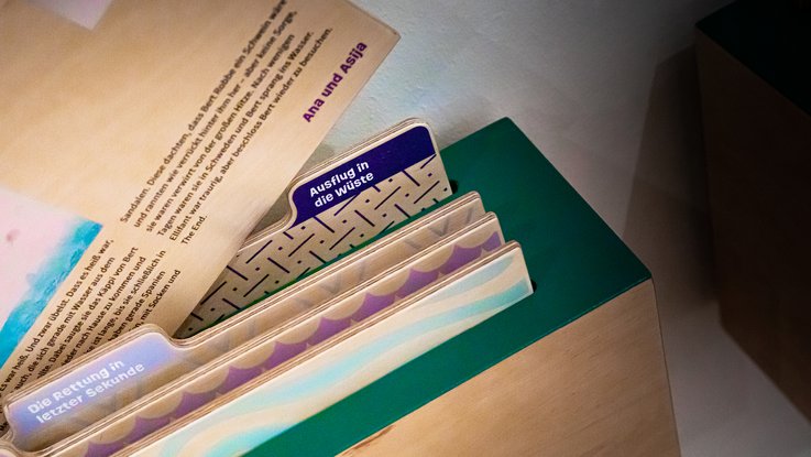 VISUELL Szenografie: Ausstellung „Spurensuche“: Detailaufnahme der Mosaik-AG. bestehend aus Holzeinschüben mit Geschichten der Kinder in einer Wandbefestigung