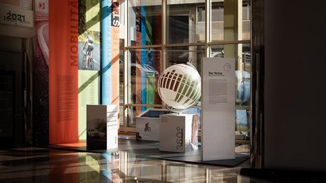 VISUELL Szenografie: Jubiläumsausstellung: Vom Rennfahrer zum Verleger, 75 Jahre Verlagsgeschichte VISUELL Szenografie: Ausstellungsrundgang: Übersicht der Ausstellung, mit Stoffbannern und Globus für die Geschichte des Verlags