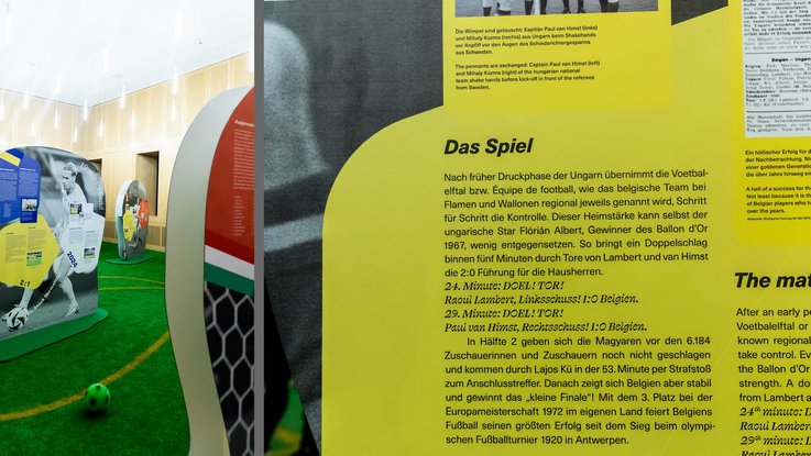 VISUELL Szenografie: EURO Legends Stuttgart: Detailaufnahme der Schrift auf gelbem Grund auf einem Aufsteller, im Hintergrund sind weitere Aufsteller sowie ein Fußball zu sehen.