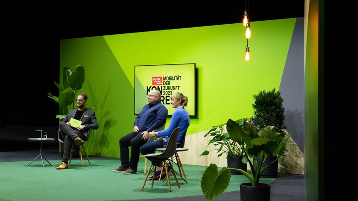 VISUELL Szenografie: Bühnenbild und Gesamtinszenierung: Drei Personen sitzen vor dem grünen Bühnenbild in einer Talk-Runde