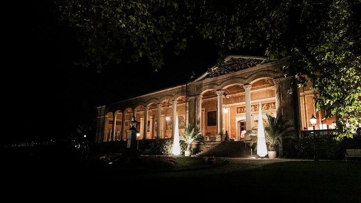 VISUELL Szenografie: Gestaltung und Realisierung des Leitsystems und der Printprodukte für die Nacht des offenen Denkmals in Baden-Baden. VISUELL Szenografie: Nacht des offenen Denkmals: Die Trinkhalle in Baden-Baden angeleuchtet bei Nacht mit Leuchtkegeln und Banner ausgestattet