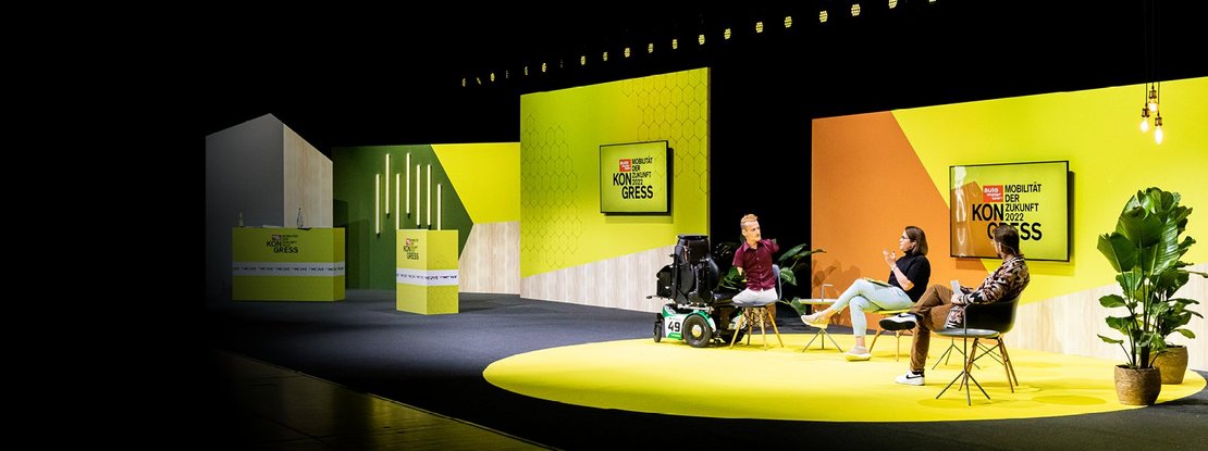 VISUELL Szenografie: Bühnenbild und Gesamtinszenierung vom AMS Kongress, Auto Motor und Sport, Motor Presse Stuttgart VISUELL Szenografie: Drei Personen unterhalten sich vor einer gelb/orangenen Wand