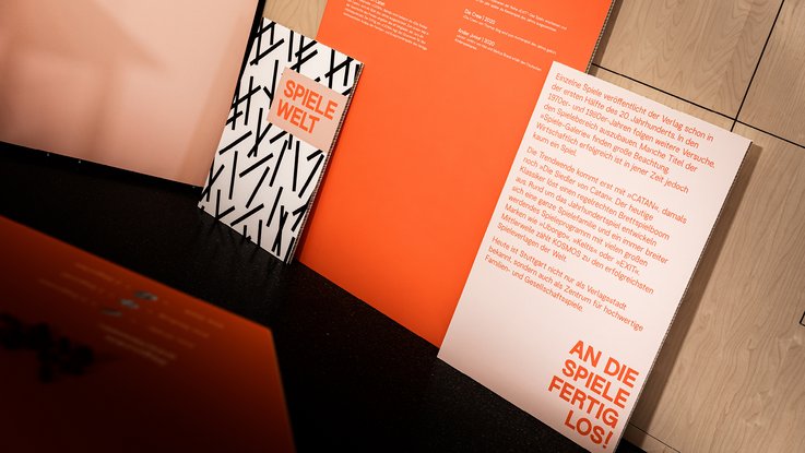 VISUELL Szenografie: 200 Jahre KOSMOS, Jubiläumsausstellung VISUELL Szenografie: Ausstellungsrundgang: Orangene Texttafeln in der Spielewelt – Aufschrift: An die Spiele fertig los!