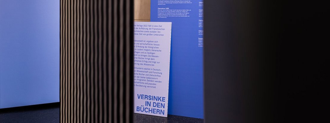 VISUELL Szenografie: Ausstellungsrundgang: zwei blaue Texttafeln – Aufschrift: Versinke in den Büchern