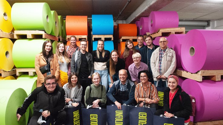 VISUELL Blogbeitrag: Weiterbildung in Innsbruck und München: Das VISUELL-Team vor großen bunten Papierrollen beim Designfestival beim Papierhersteller Gmund