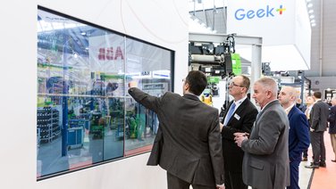VISUELL Szenografie: Messestand STAHL CraneSystems: Vier Besucher bedienen die interaktive Medieninstallation über einen Touchscreen  