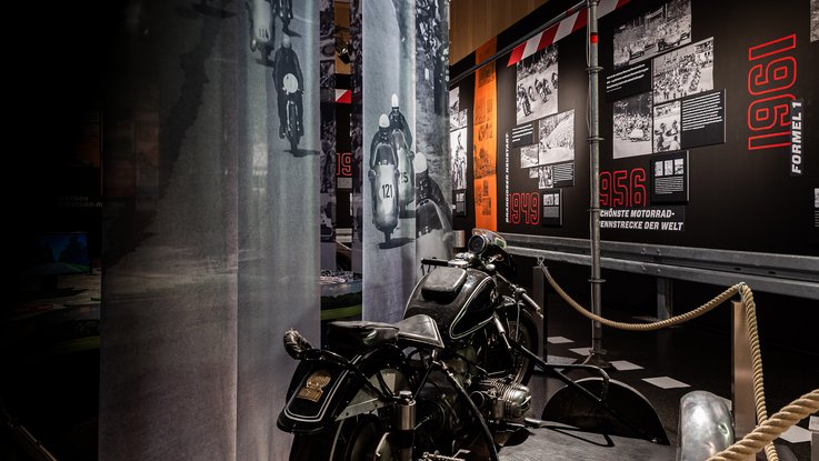 VISUELL Szenografie: Mythos Solitude: Motorrad in der Mitte des Bildes und schwarz weiße Stoffbanner hängen von der Decke darüber