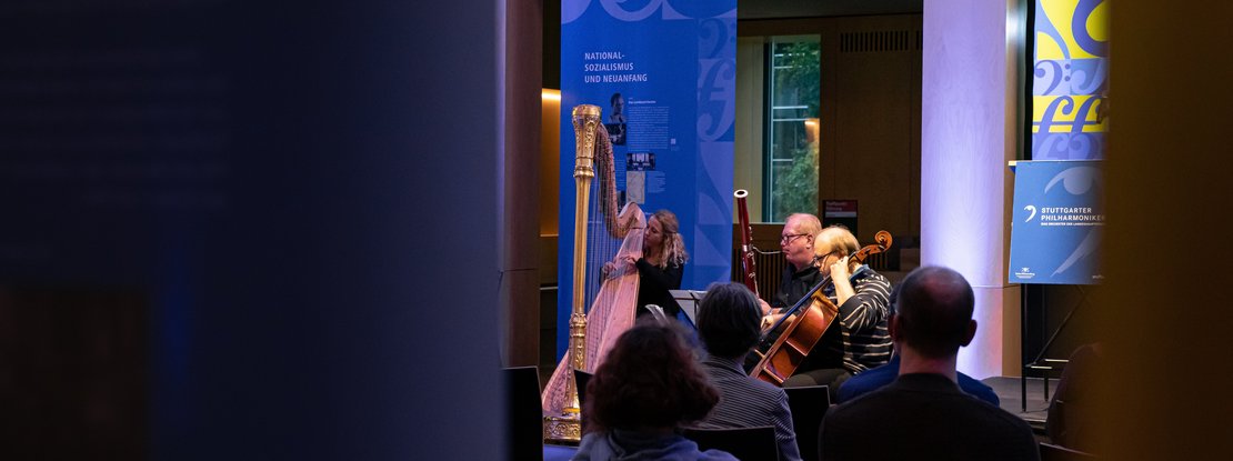 VISUELL Szenografie: Jubiläumsausstellung: Einblick in die Eröffnungsveranstaltung über die Schultern des Publikums auf die Musikerinnen und Musiker des Orchesters