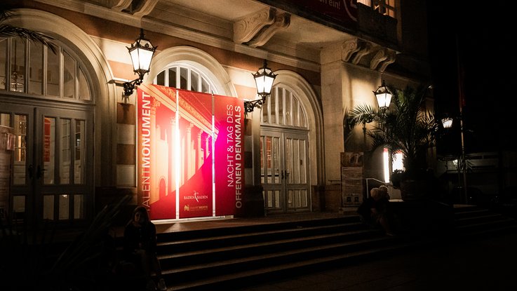 VISUELL Szenografie: Gestaltung und Realisierung des Leitsystems und der Printprodukte für die Nacht des offenen Denkmals in Baden-Baden. VISUELL Szenografie: Nacht des offenen Denkmals: Die Liederhalle in Baden-Baden angeleuchtet bei Nacht mit Leuchtkegeln und Banner ausgestattet