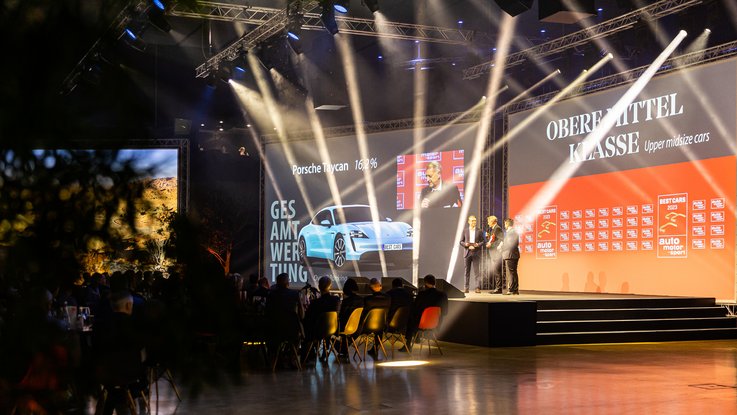 VISUELL Szenografie: BEST CARS 2023: Vier Leinwände werden bespielt - Aufschrift: Gesamtwertung Obere Mittelklasse und ein Foto eines Porsche Taycan