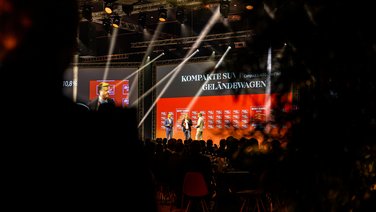 VISUELL Szenografie: BEST CARS 2023: Drei Leute auf der Bühne im Gespräch - Aufschrift Leinwand: Kompakte SUV Geländewagen