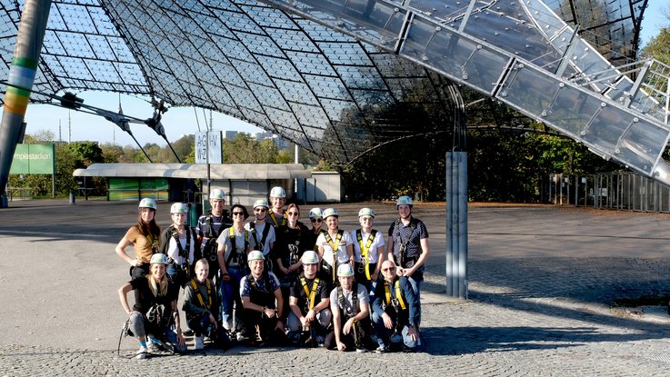 VISUELL Blogbeitrag: Weiterbildung in Innsbruck und München: Das VISUELL-Team steht mit Helm und Gurt vor dem Olympiastadion in München