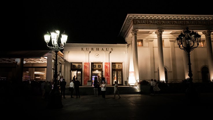 VISUELL Szenografie: Gestaltung und Realisierung des Leitsystems und der Printprodukte für die Nacht des offenen Denkmals in Baden-Baden. VISUELL Szenografie: Nacht des offenen Denkmals: Das Kurhaus in Baden-Baden angeleuchtet bei Nacht mit Leuchtkegeln und Banner ausgestattet