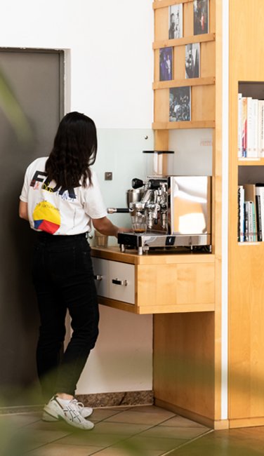 VISUELL Blogbeitrag: Kaffeegenuss: Mitarbeiterin Aline steht an der Kaffee-Ecke bei VISUELL im Studio