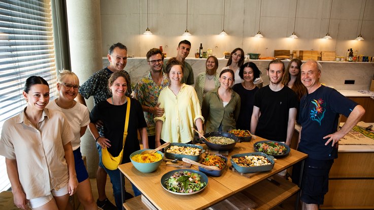 VISUELL Blogbeitrag: Auf Weiterbildung in der Rapunzelwelt. Wir lernen nachhaltige Anbauweisen kennenlernen. VISUELL Blogbeitrag: Weiterbildung in der Rapunzelwelt: Das VISUELL-Team steht vor einem Tisch voller angerichteten Rezepte