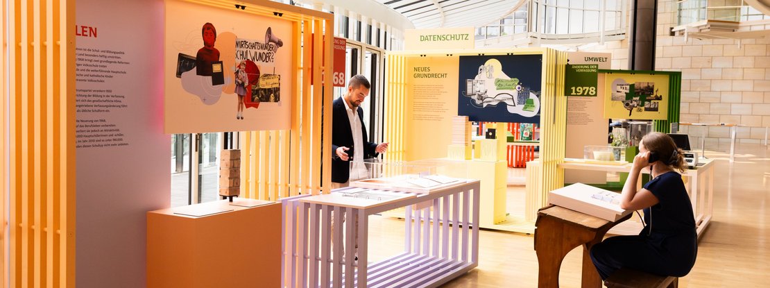 VISUELL Szenografie: Wanderausstellung „Jubiläum. 75 Jahre Verfassung NRW“ für die Stiftung Haus der Geschichte Nordrhein-Westfalen VISUELL Szenografie: Wanderausstellung: Besucher:innen interagieren mit farbig gestalteten Modulen zu Themen Bildung, Datenschutz und Umwelt. Lichtdurchfluteter Raum mit klarer, modularer Gestaltung und grafischen Wandelementen.